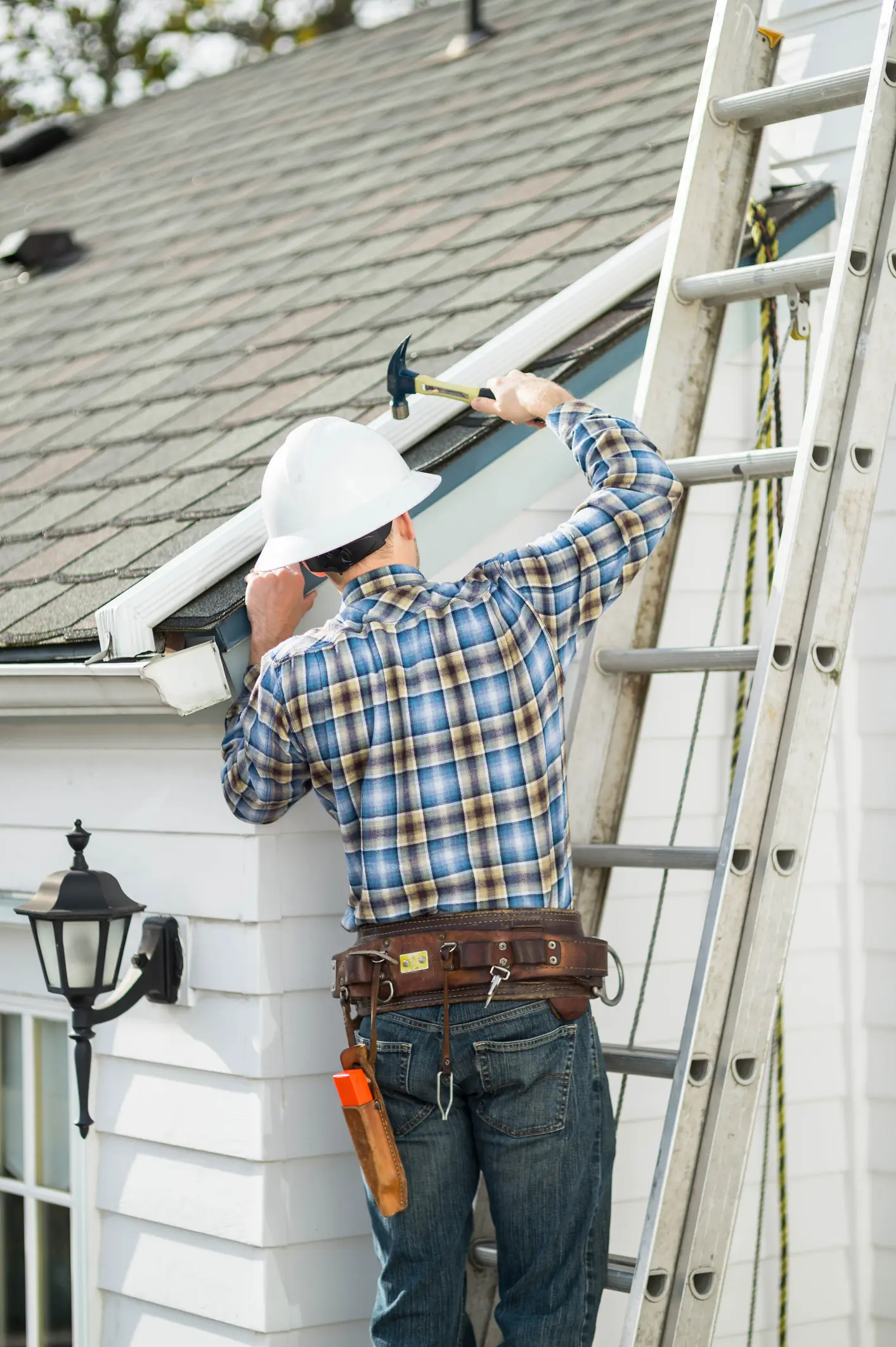 Man on a ladder holding a hammer toward the roof.